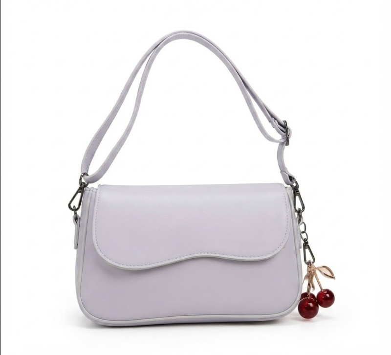 A light lavender purple shoulder bag with a curved flap, adjustable strap, and a cherry charm hanging from the side, shown on a plain white background.
